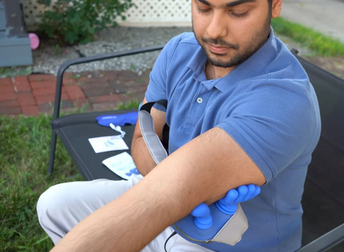 The CHOOSE-US massager being used on the forearm, demonstrating use on areas beyond the neck
